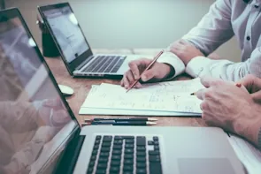 Persona con una penna in mano accanto a un computer portatile